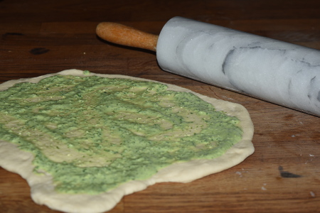 Dough rolled out with a generous layer of pesto spread across it